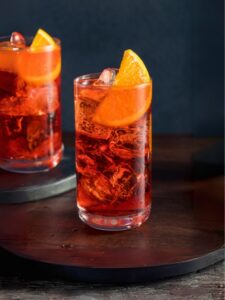 Cocktail Americano, boisson avec du vermouth et du Campari, serivi dans un verre décoré avec des zestes d'oranges et des glaçons