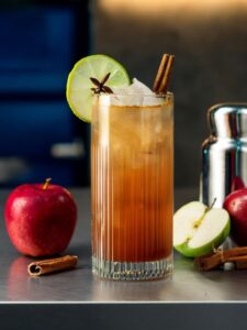 cocktail cinnamon sky servi dans un verre highball avec de la pomme et de la cannelle