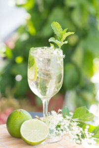 Cocktail Hugo Spritz, préparé avec du prosecco, de l'eau gazeuse, de la liqueur de sureau, garni de feuilles de menthe fraîche, d'une rondelle de citron et de fleurs pour une boisson rafraîchissante et parfumée servie dans un verre piscine.