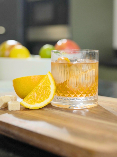 CCocktail Old Fashionned à base de blended scotch whisky, de bitter et d'eau gazeuse, servi dans un verre garni d'un zeste de citron