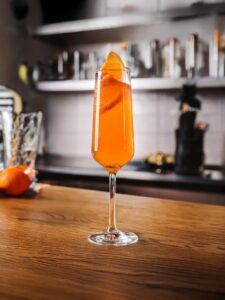 cocktail barbotage posé sur un plan de travail en bois dans une cuisine. Le cocktail est orange et pétillant