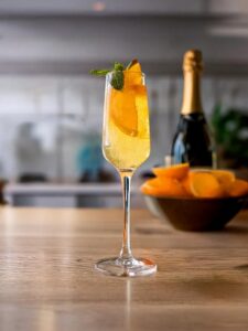 cocktail au champagne et aux oranges décoré d'une feuille de menthe fraiche sur le dessus.